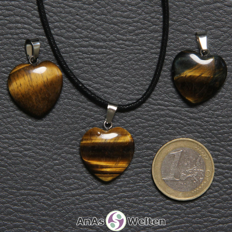 Drei Herzanhänger aus Tigerauge nebeneinander. Einer befindet sich an einem schwarzen gewachsten Baumwollband.