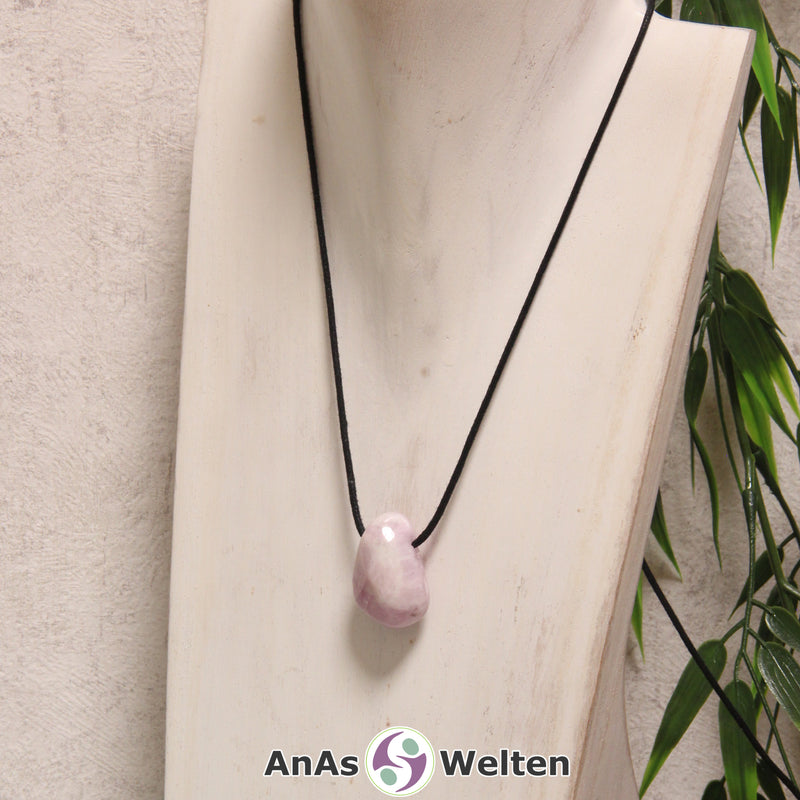 Ein rosa Kunzit gebohrter Trommelstein an einem schwarzen Baumwollband, der um eine helle Büste gehängt wurde.