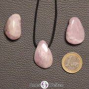 Drei rosa Kunzit gebohrte Trommelsteine nebeneinander. Einer befindet sich an einem schwarzen gewachsten Baumwollband.