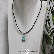 Ein blauer Larimar Stein mit Öse an einem schwarzen Baumwollband, der um eine helle Büste gehängt wurde.