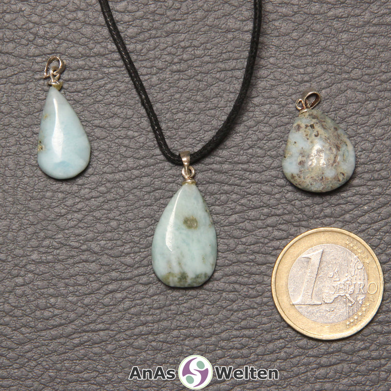 Drei blaue Larimar Steine mit Öse nebeneinander. Einer befindet sich an einem schwarzen gewachsten Baumwollband.