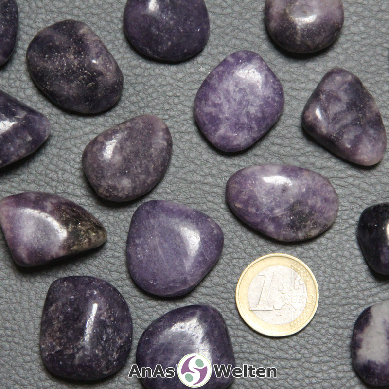 Das Bild zeigt einen Lepidolith Trommelstein anhand von mehreren Beispielsteinen. Die Edelsteine haben eine hell- bis dunkellila Farbe mit einem unregelmäßigen Muster.