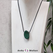 Ein grüner Malachit gebohrter Trommelstein an einem schwarzen Baumwollband, der um eine helle Büste gehängt wurde.