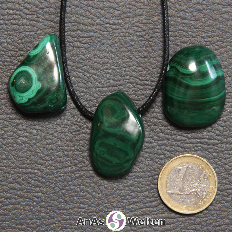 Drei grüne Malachit gebohrte Trommelsteine nebeneinander. Einer befindet sich an einem schwarzen gewachsten Baumwollband.