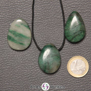 Drei grün-weiße Prasem gebohrte Trommelsteine nebeneinander. Einer befindet sich an einem schwarzen gewachsten Baumwollband.