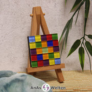 Das Bild zeigt ein Sator Quadrat Mosaik ohne Rahmen. Die Fliesen sind Glasfliesen in zwei verschiedenen Blautönen, Gelb, Lila, Rot, zwei Grüntönen und Orange. Jeder Buchstabe auf dem Sator Quadrat wird durch eine andere Fliesenfarbe dargestellt.
