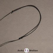 Ein schwarzes Baumwollband mit 1 mm Dicke, bei dem man den Schiebeknoten sieht, mit dem es zur Kette gebunden wurde.