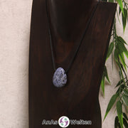 Ein gebohrter Sodalith an einem Baumwollband. Der Edelstein hat eine dunkelblau-weiße Farbe mit unregelmäßiger Musterung.