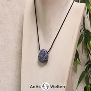 Ein blau-weiße Sodalith gebohrter Trommelstein an einem schwarzen Baumwollband, der um eine helle Büste gehängt wurde.