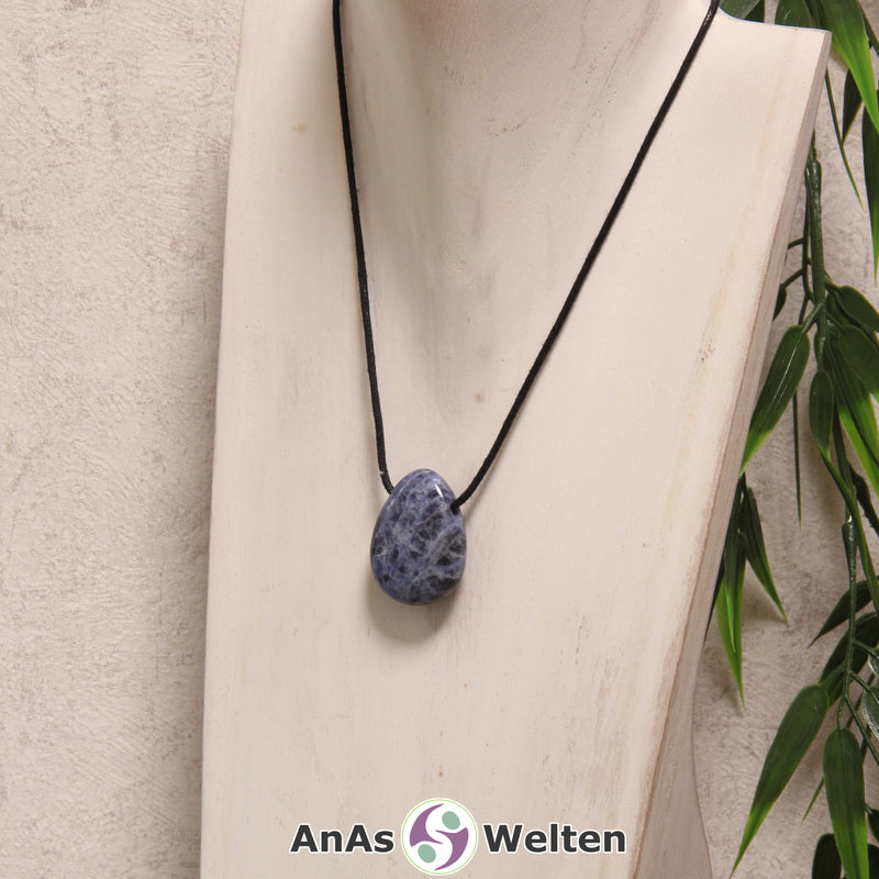 Ein blau-weiße Sodalith gebohrter Trommelstein an einem schwarzen Baumwollband, der um eine helle Büste gehängt wurde.