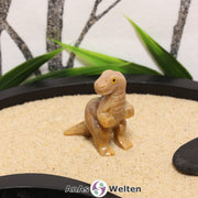 Das Bild zeigt einen Speckstein T-Rex klein. Die Specksteinfigur steht auf den Hinterbeinen und hat den Kopf zur Seite gerichtet. Die Augen bestehen aus einem anderen Material, sodass sie besser zur Geltung kommen, und die Schuppen und Krallen sind durch Einkerbungen im Stein angedeutet.