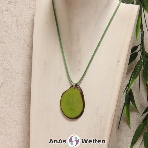 Das Produktbild zeigt die Tagua-Nuss-Schmuck Kette apfelgrün. Zu sehen ist eine hellgrüne Tagua-Nuss-Scheibe, die mit einer Edelstahlöse an einem grünen Baumwollband befestigt ist. Die Nuss-Scheibe hat einen dunklen Rand und eine glänzende Oberfläche.