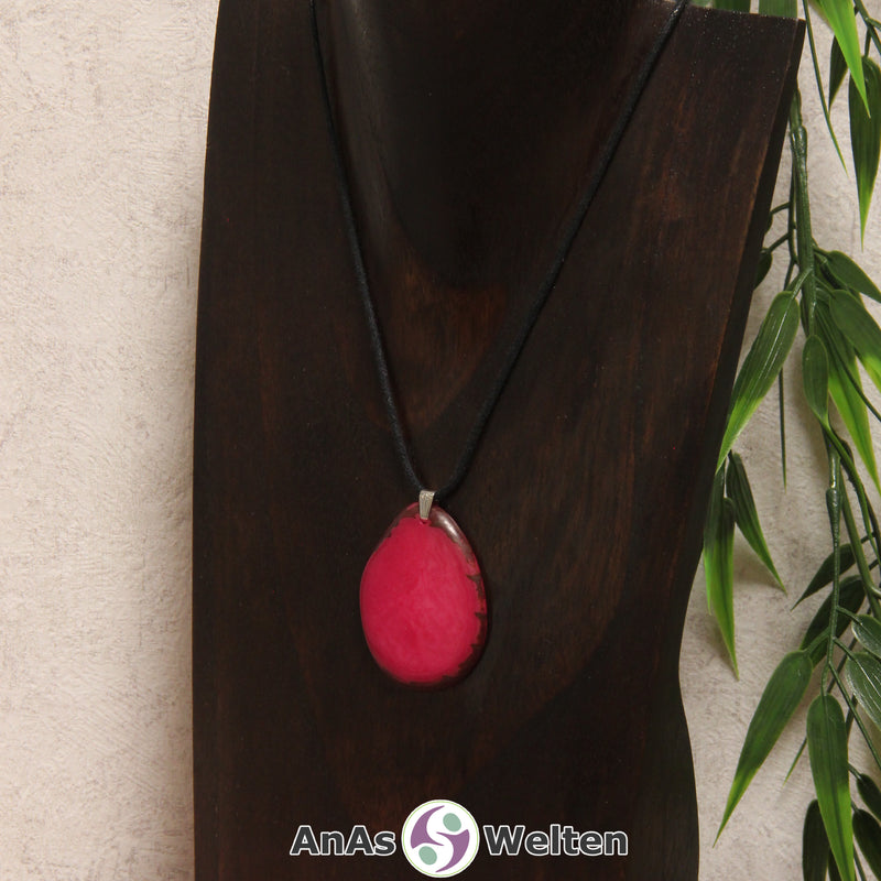 Eine fuchsiafarbene Tagua-Nuss Schmuck Kette mit Öse mit einem schwarzen Baumwollband an einer dunklen Büste.