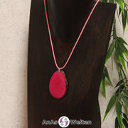 Eine fuchsiafarbene Tagua-Nuss Schmuck Kette mit Öse mit einem rosa Baumwollband an einer dunklen Büste.