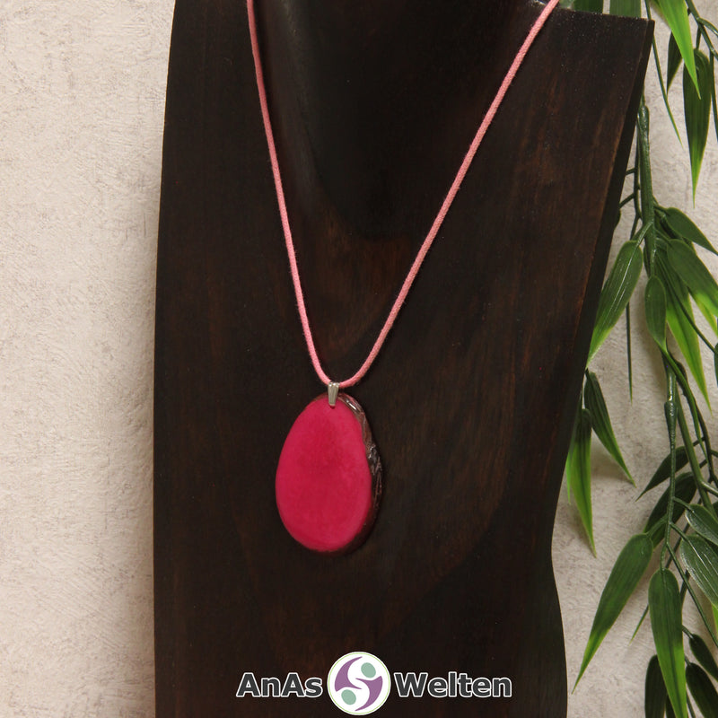 Eine fuchsiafarbene Tagua-Nuss Schmuck Kette mit Öse mit einem rosa Baumwollband an einer dunklen Büste.