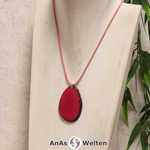 Das Produktbild zeigt die Tagua-Nuss-Schmuck Kette fuchsia. Zu sehen ist eine pinke Tagua-Nuss-Scheibe, die mit einer Edelstahlöse an einem rosa Baumwollband befestigt ist. Die Nuss-Scheibe hat einen dunklen Rand und eine glänzende Oberfläche.