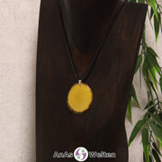 Eine gelb gefärbte Tagua-Nuss Schmuck Kette mit Öse mit einem schwarzen Baumwollband an einer dunklen Büste.