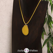 Eine gelb gefärbte Tagua-Nuss Schmuck Kette mit Öse mit einem gelben Baumwollband an einer dunklen Büste.