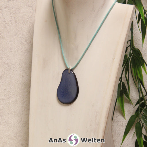 Das Produktbild zeigt die Tagua-Nuss-Schmuck Kette hellblau. Zu sehen ist eine blaue Tagua-Nuss-Scheibe, die mit einer Edelstahlöse an einem türkisen Baumwollband befestigt ist. Die Nuss-Scheibe hat einen dunklen Rand und eine glänzende Oberfläche.