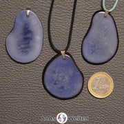 Drei hellblau gefärbte Tagua-Nuss-Scheiben mit Metallöse. Zwei sind an einem schwarzen bzw. türkisen Baumwollband.