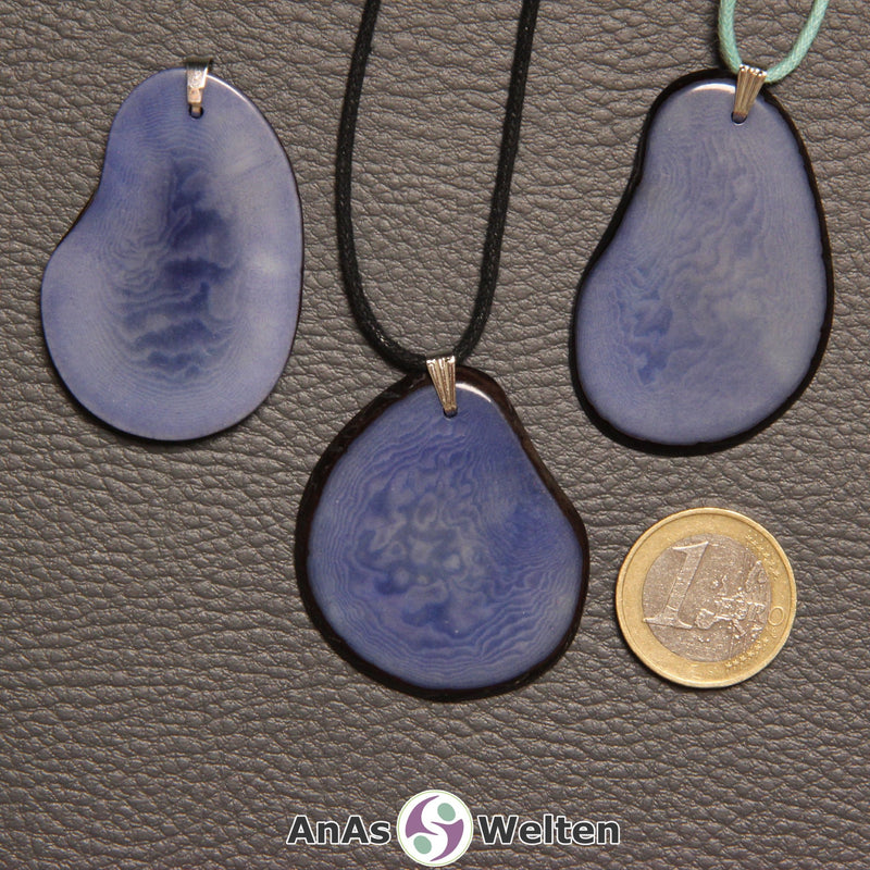 Drei hellblau gefärbte Tagua-Nuss-Scheiben mit Metallöse. Zwei sind an einem schwarzen bzw. türkisen Baumwollband.