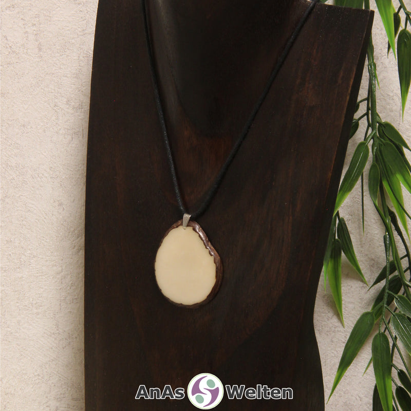 Eine naturfarbene Tagua-Nuss Schmuck Kette mit Öse mit einem schwarzen Baumwollband an einer dunklen Büste.