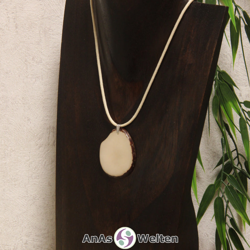 Das Produktbild zeigt die Tagua-Nuss-Schmuck Kette himmlblau. Zu sehen ist eine hellblaue Tagua-Nuss-Scheibe, die mit einer Edelstahlöse an einem beigen Baumwollband befestigt ist. Die Nuss-Scheibe hat einen dunklen Rand und eine glänzende Oberfläche.