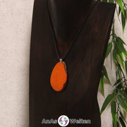 Eine orange gefärbte Tagua-Nuss Schmuck Kette mit Öse mit einem schwarzen Baumwollband an einer dunklen Büste.