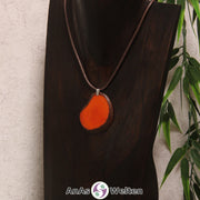 Eine orange gefärbte Tagua-Nuss Schmuck Kette mit Öse mit einem braunen Baumwollband an einer dunklen Büste.