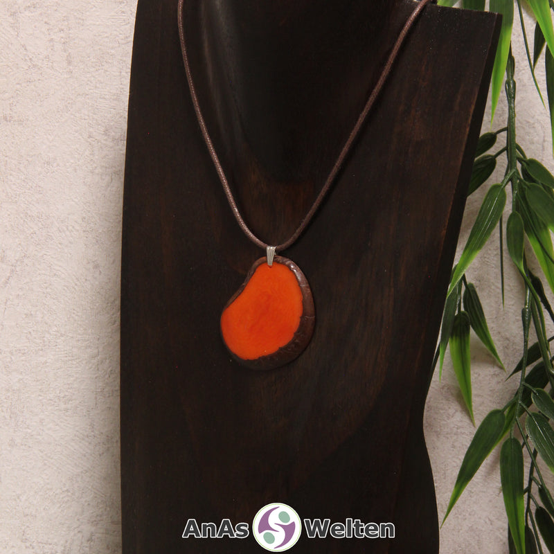 Eine orange gefärbte Tagua-Nuss Schmuck Kette mit Öse mit einem braunen Baumwollband an einer dunklen Büste.