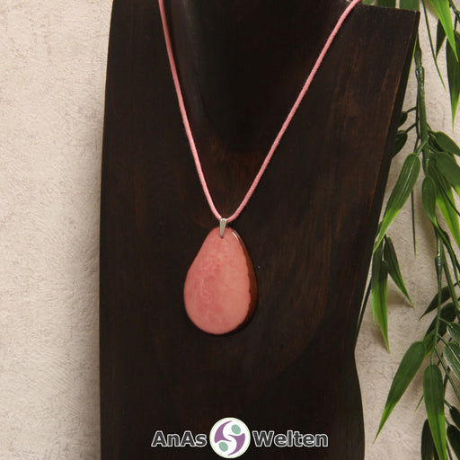 Das Produktbild zeigt die Tagua-Nuss-Schmuck Kette rosa. Zu sehen ist eine rosa Tagua-Nuss-Scheibe, die mit einer Edelstahlöse an einem rosa Baumwollband befestigt ist. Die Nuss-Scheibe hat einen dunklen Rand und eine glänzende Oberfläche.
