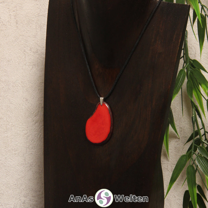 Eine rote Tagua-Nuss Schmuck Kette mit Öse mit einem schwarzen Baumwollband an einer dunklen Büste.