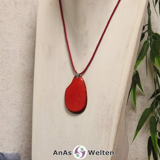 Das Produktbild zeigt die Tagua-Nuss-Schmuck Kette rot. Zu sehen ist eine rote Tagua-Nuss-Scheibe, die mit einer Edelstahlöse an einem roten Baumwollband befestigt ist. Die Nuss-Scheibe hat einen dunklen Rand und eine glänzende Oberfläche.