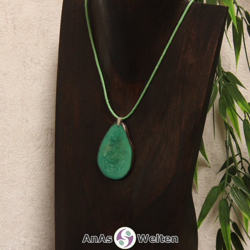 Das Produktbild zeigt die Tagua-Nuss-Schmuck Kette seegrün. Zu sehen ist eine grüne Tagua-Nuss-Scheibe, die mit einer Edelstahlöse an einem grünen Baumwollband befestigt ist. Die Nuss-Scheibe hat einen dunklen Rand und eine glänzende Oberfläche.