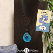 Eine türkis gefärbte Tagua-Nuss Sternzeichen Kette mit silberfarbenem Fische-Symbol und Lavakugel an einer dunklen Büste.