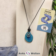 Eine türkis gefärbte Tagua-Nuss Sternzeichen Kette mit silberfarbenem Fische-Symbol und Lavakugel an einer hellen Büste.