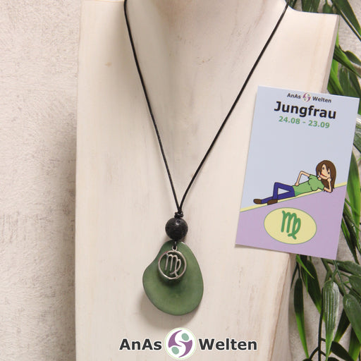 Das Produktbild für die Tagua-Nuss-Schmuck Sternzeichen-Kette Jungfrau zeigt eine in grün gefärbte Tagua-Nuss-Scheibe an einem schwarzen Baumwollband, vor der ein silberfarbener Anhänger mit dem Sternzeichensymbol der Jungfrau befestigt ist. Die Nuss-Scheibe hat einen dunklen Rand und eine glänzende Oberfläche. Direkt darüber befindet sich eine Lavakugel. Rechts neben der Kette sieht man außerdem die Sternzeichen Jungfrau Karte von AnAs Welten.