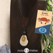 Eine naturfarbene Tagua-Nuss Sternzeichen Kette mit goldfarbenem Krebs-Symbol und Lavakugel an einer dunklen Büste.
