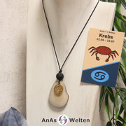 Eine naturfarbene Tagua-Nuss Sternzeichen Kette mit goldfarbenem Krebs-Symbol und Lavakugel an einer hellen Büste.