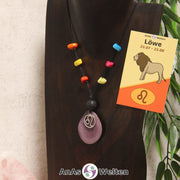 Eine lila Tagua-Nuss Sternzeichen Kette mit bunten Taguasplittern, silber Löwe-Symbol und Lavakugel an einer dunklen Büste.