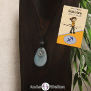 Eine himmelblau gefärbte Tagua-Nuss Sternzeichen Kette mit silberfarbenem Schütze-Symbol und Lavakugel an einer dunklen Büste.