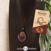 Eine violett gefärbte Tagua-Nuss Sternzeichen Kette mit goldfarbenem Skorpion-Symbol und Lavakugel an einer dunklen Büste.