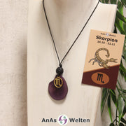 Eine violett gefärbte Tagua-Nuss Sternzeichen Kette mit goldfarbenem Skorpion-Symbol und Lavakugel an einer hellen Büste.