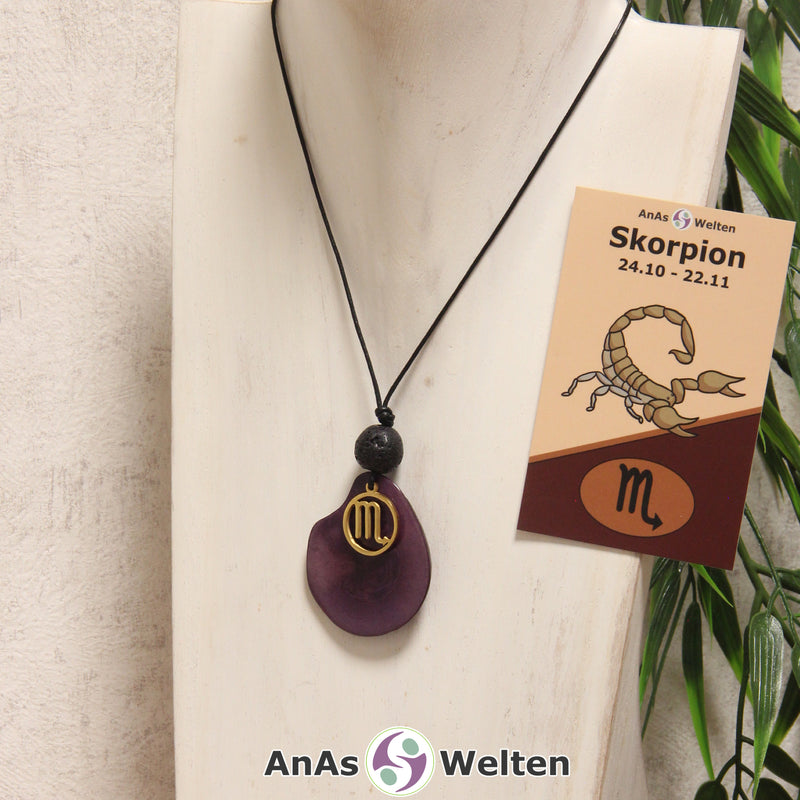 Eine violett gefärbte Tagua-Nuss Sternzeichen Kette mit goldfarbenem Skorpion-Symbol und Lavakugel an einer hellen Büste.