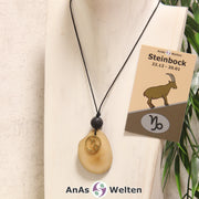 Eine beige gefärbte Tagua-Nuss Sternzeichen Kette mit goldfarbenem Steinbock-Symbol und Lavakugel an einer hellen Büste.