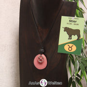 Eine rosa gefärbte Tagua-Nuss Sternzeichen Kette mit silberfarbenem Stier-Symbol und Lavakugel an einer dunklen Büste.