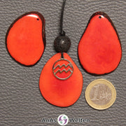 Drei Tagua-Nuss-Scheiben in rot. EIne davon ist als Kette mit Lavakugel und Wassermann-Symbol gebunden.