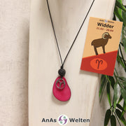 Eine fuchsiafarbene Tagua-Nuss Sternzeichen Kette mit silberfarbenem Widder Symbol und Lavakugel an einer hellen Büste.