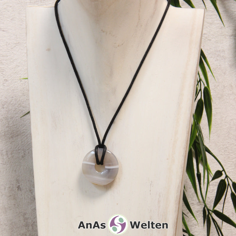 Ein Achat Donut als Kette an einem schwarzen gewachsten Baumwollband um eine helle Büste.
