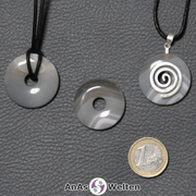 Drei Achat Donuts nebeneinander. Einer an einem Baumwollband, ein anderer an einem Donut-Halter mit Baumwollband.